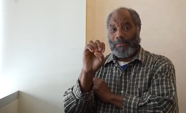 A man sitting and signing at the camera